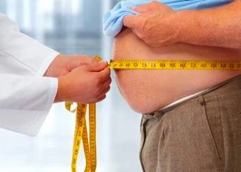 Imagen de un doctor nutricionista con una cinta métrica midiendo el abdomen de una persona obesa. Los efectos nocivos de las dietas altas en grasas.