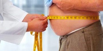 Imagen de un doctor nutricionista con una cinta métrica midiendo el abdomen de una persona obesa. Los efectos nocivos de las dietas altas en grasas.